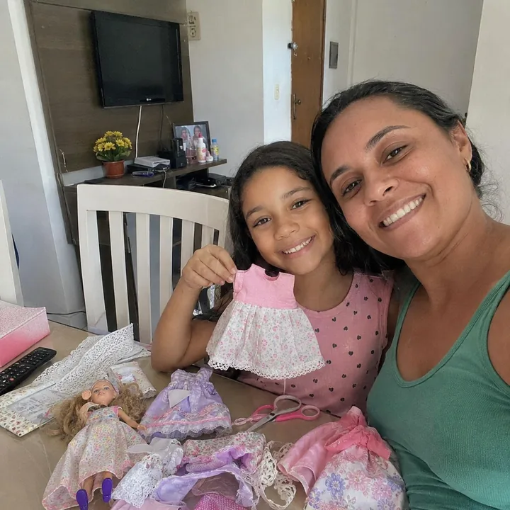 Mãe e filha mostrando vestido de boneca feito em casa