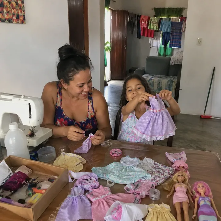 Mãe observando a filha apresentar vestido de boneca costurado em casa